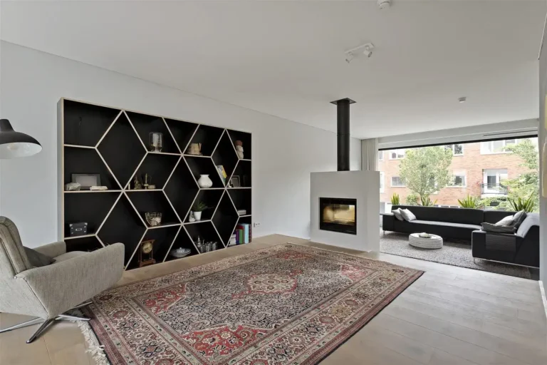 Vastgoedfotografie van een design woonkamer met een opvallende geometrische zwarte boekenkast, een doorkijkhaard, een Perzisch tapijt en een lichte houten vloer.