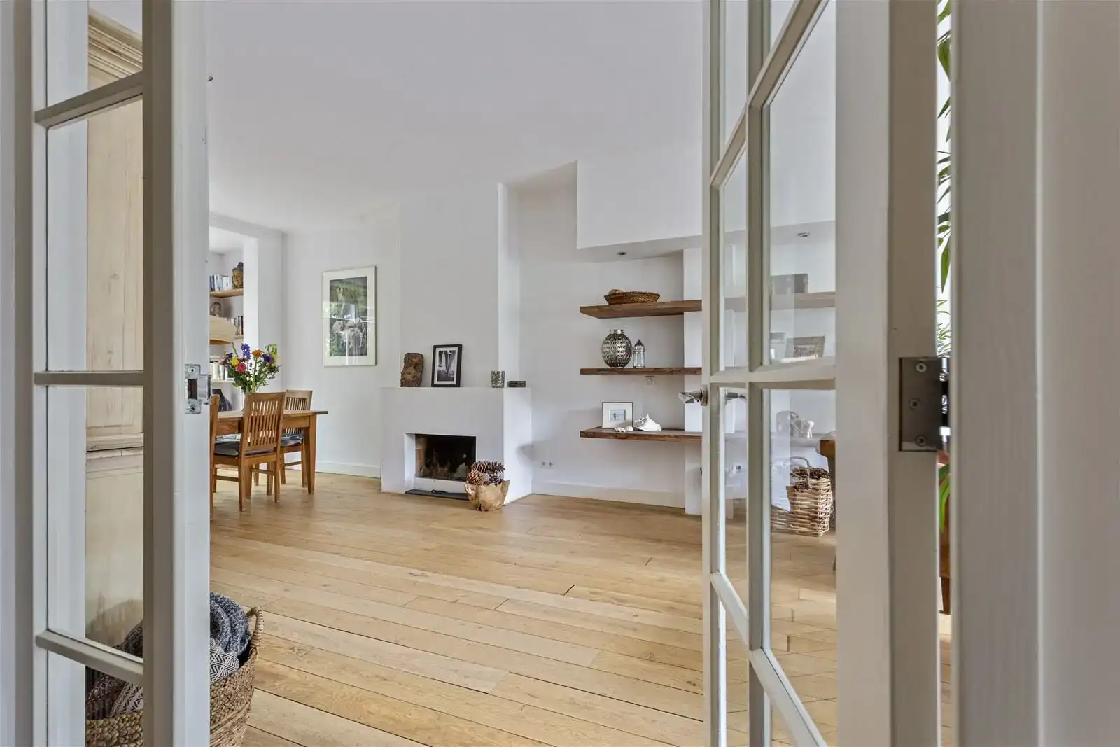 Vastgoedfotografie van een lichte woonkamer met een open haard, eikenhouten vloer en ingebouwde nissen, gefotografeerd door openslaande witte suite-deuren met glas.