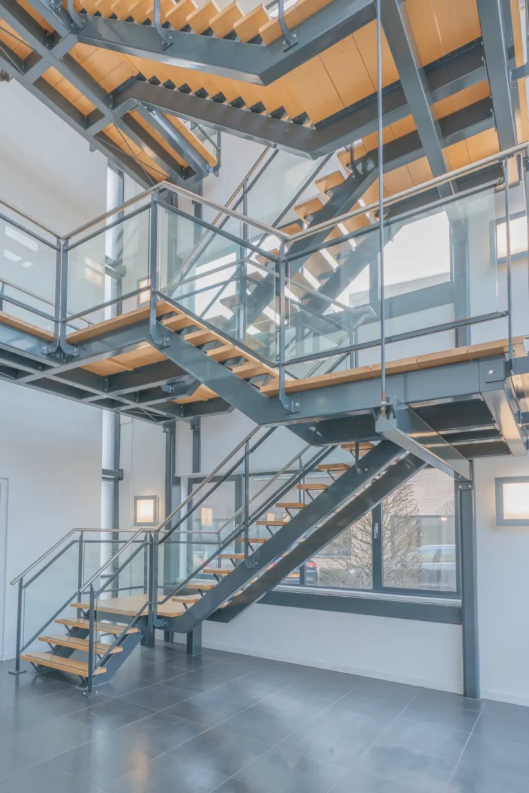 Architectuurfotografie van een modern trappenhuis in een kantoorpand met een stalen constructie, houten traptreden en glazen balustrades.