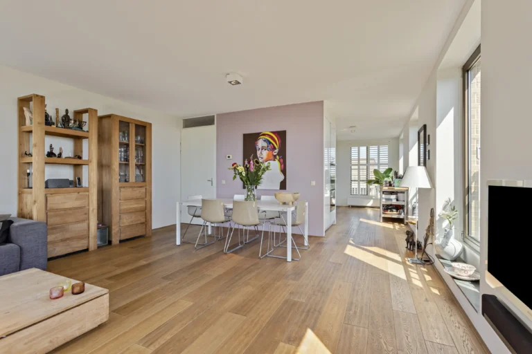 Vastgoedfotografie van een lichte, ruime woonkamer met een eethoek, houten vloer, moderne meubels en grote ramen met natuurlijke lichtinval.
