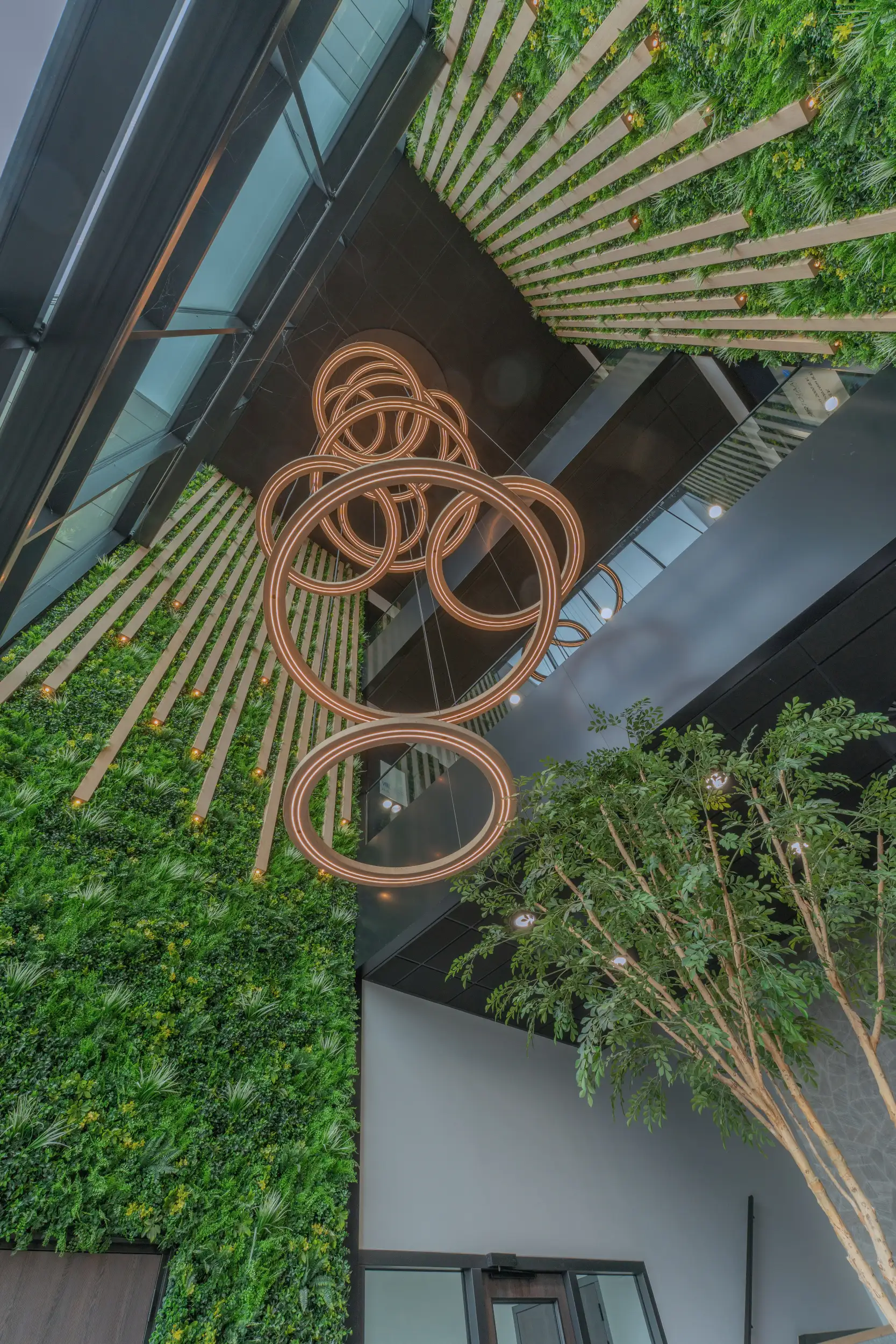 Interieurfotografie van een high-end kantoorentree met een hoog atrium, biofiel design, groene plantenwanden en een grote design ringlamp.